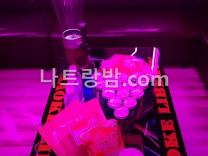 분홍 조명 아래 얼음통과 잔을 올린 리버티 가라오케 테이블