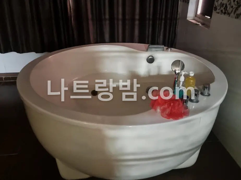 어두운 커튼 앞에 흰 원형 욕조를 놓은 도쿄마사지 욕실
